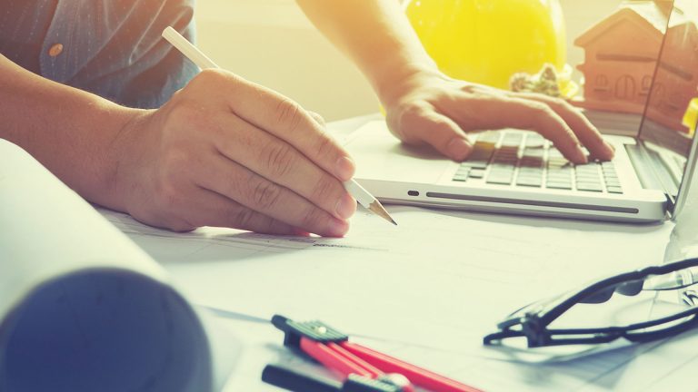 Image of a contractor working on a laptop holding a pencil